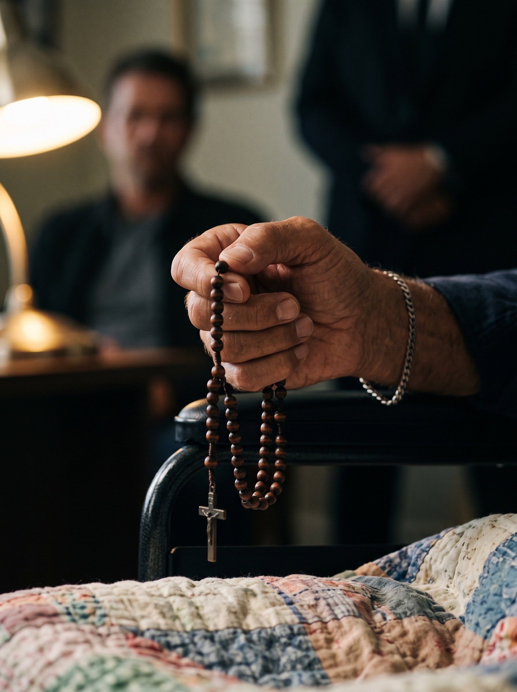 Jimmy Flynn’s hand holding a wooden rosary above the quilt covering his legs